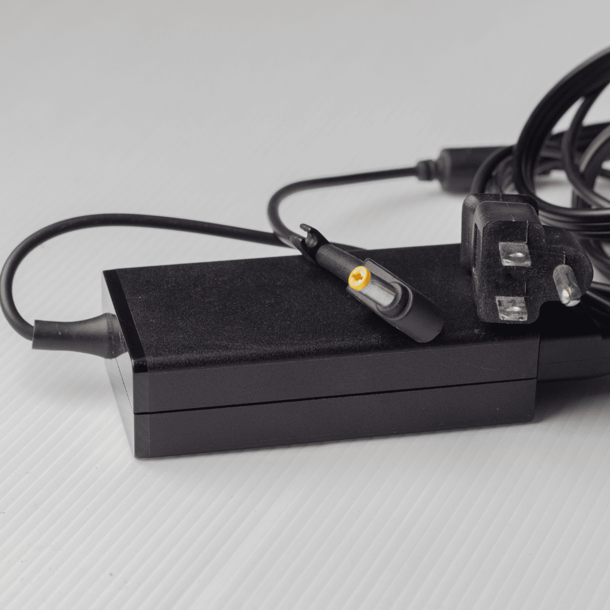 "Black laptop adapter with a compact design, featuring a power input for wall sockets and an output cable for charging laptops efficiently."